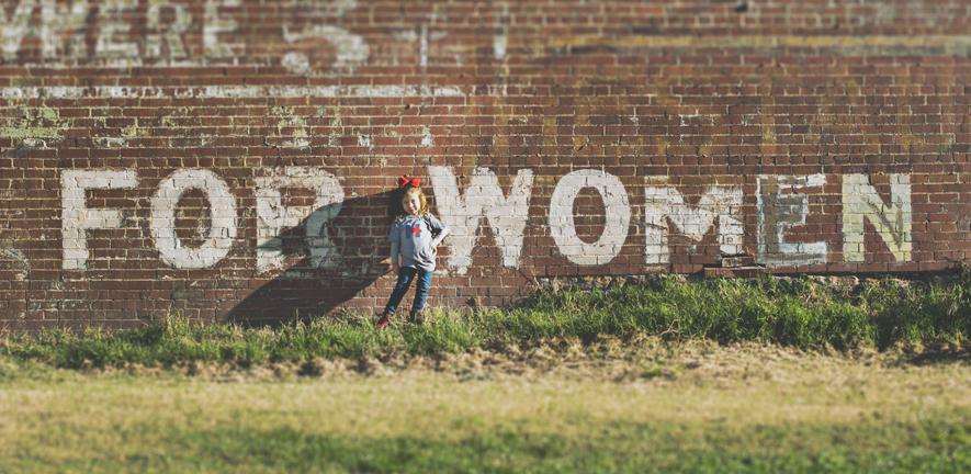For women - Photo by Katherine Hanlon on Unsplash girl standing in front of a red brick wall which has grafitti on saying "for women"