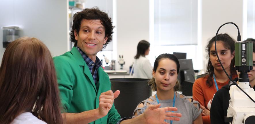 Dr Tim Weil talking to year 12 students in the lab as part of an outreach event Dr Tim Weil in a green demonstrator's lab coat talking to year 12 students in the lab at an outreach event