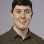 Photo of a man smilling wearing a green button-up shirt.