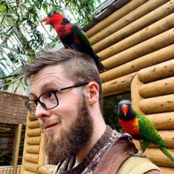 Photo of Tom Jameson with parrots on his head and shoulders